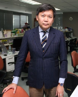 This is a picture of Thai journalist Pravit Rojanaphruk standing in the offices of a newsroom. 